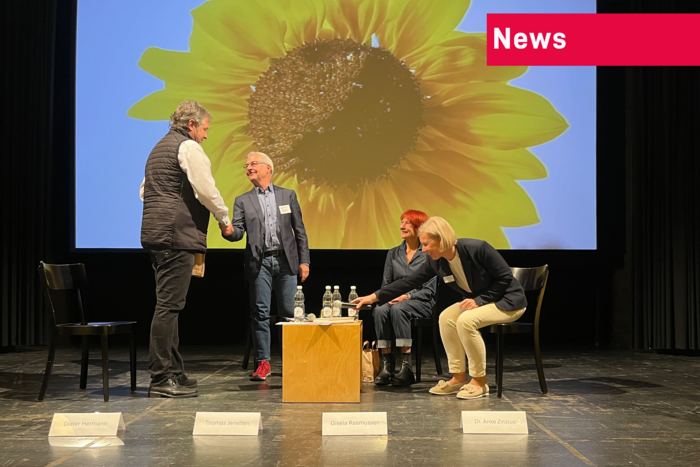 Foto der Podiumsdiskussion mit Sonnenblume im Hintergrund